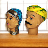 A set of two hand-painted clay puppet heads, one depicting a male character with a yellow turban and the other a female character with a blue and gold headdress, representing traditional Rajasthani aesthetics.