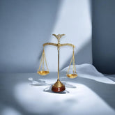 A decorative metal traditional old goldsmith weight scale known as tarazu, with a balance and two scales, against a light background.