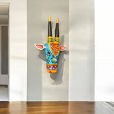 Decorative wall art of a colorful animal head with long horns on a plain wall.
