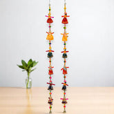 Two sets of wooden puppet hangings with colorful accents, displayed against a neutral background with a plant to the side.