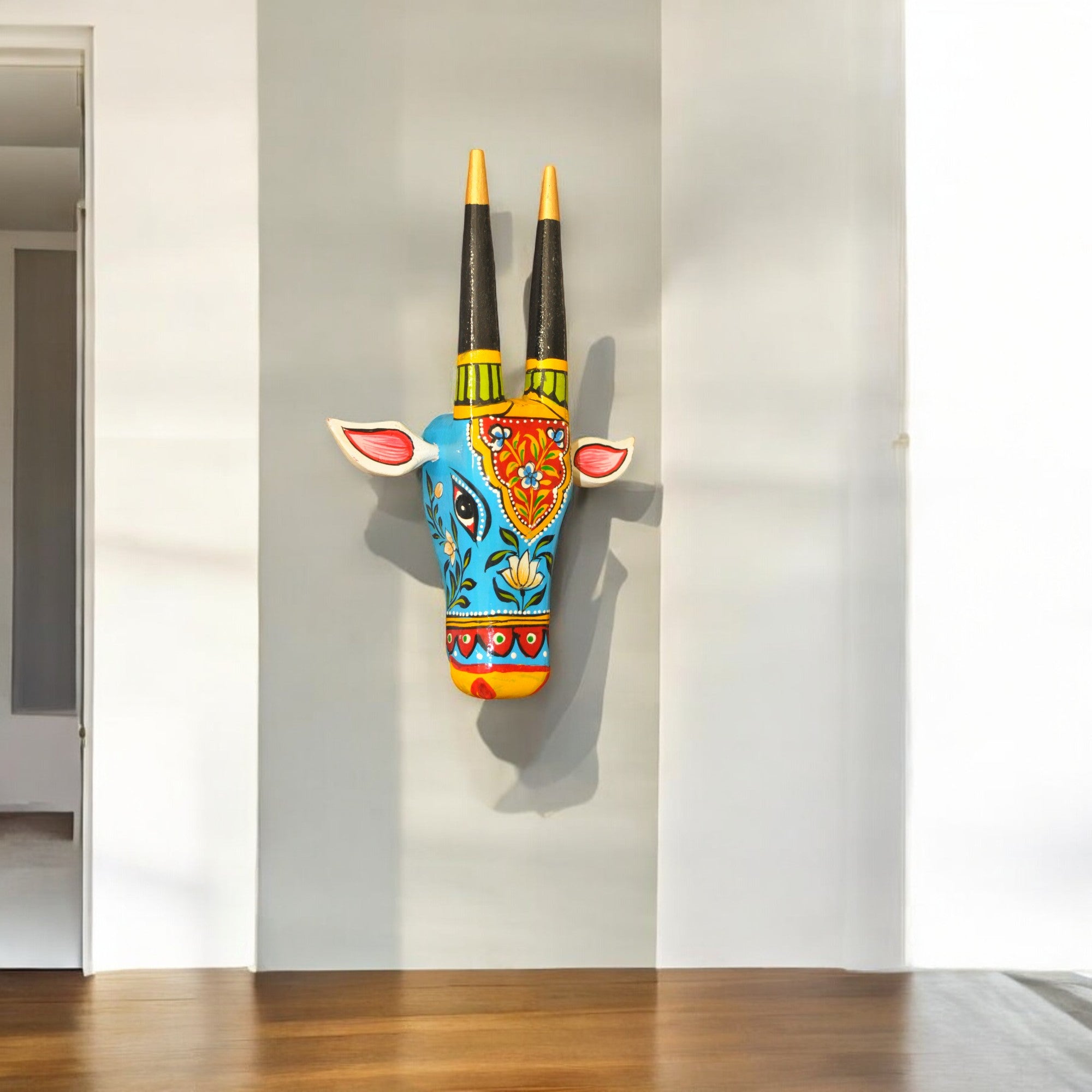 Decorative wall art of a colorful animal head with long horns on a plain wall.